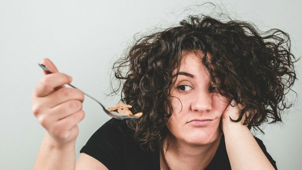 Tired woman resting her head on her hand while holding a spoonful of cereal she has no appetite to eat