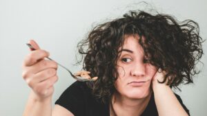 Tired woman resting her head on her hand while holding a spoonful of cereal she has no appetite to eat